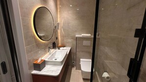 Ein modernes Badezimmer mit Marmorwand, rundem Spiegel, Waschbecken und Toilette.