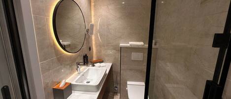Un baño moderno con pared de mármol, un espejo redondo, un lavabo y un inodoro.