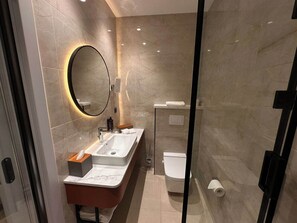 A modern bathroom with a marble wall, a round mirror, a sink, and a toilet. - Mercure Tashkent North (Tashkent)
