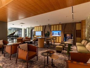 A spacious lobby with a grand piano, comfortable seating, a large TV screen, and a decorative wall. - Mercure Tashkent North (Tashkent)