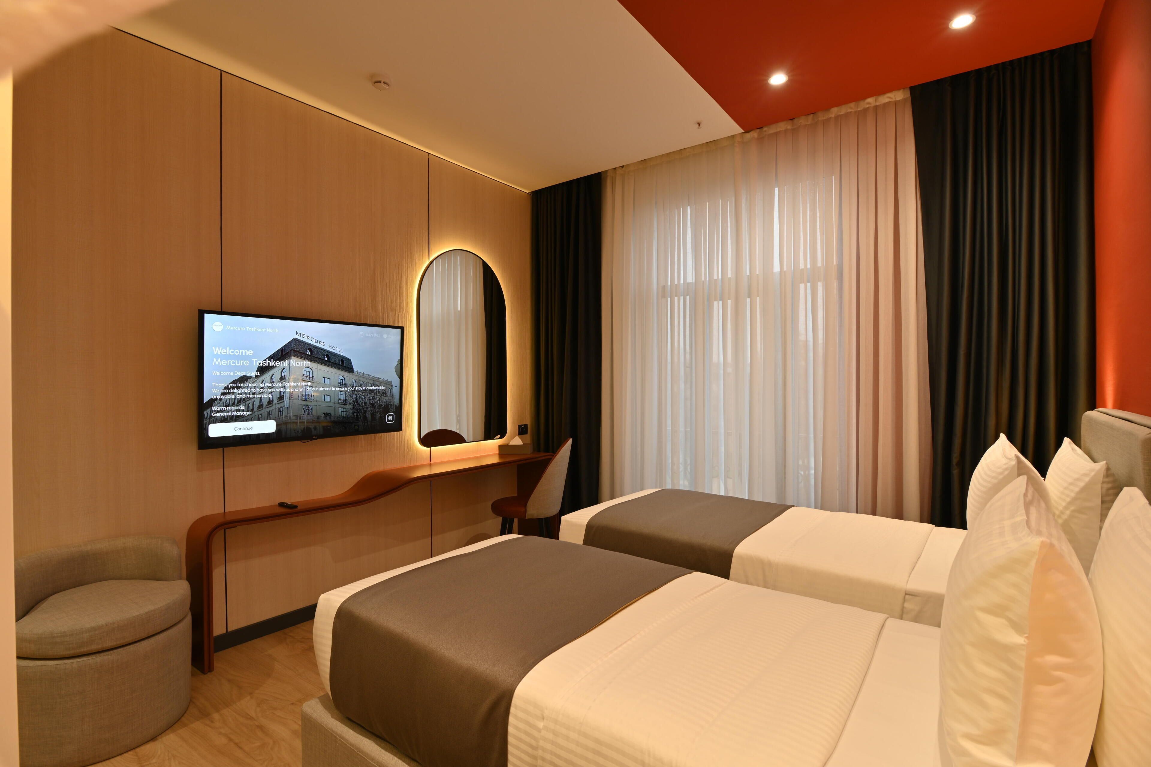 A hotel room with two beds, a TV, a mirror, and a desk.