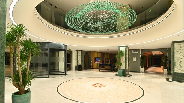 Eine geräumige Lobby mit einem kreisförmigen Muster auf dem Boden, einem Flügel und einem markanten, grünen Chandelier.