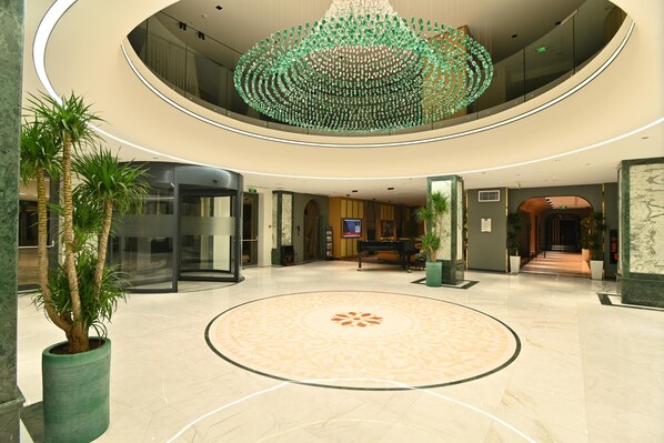 A spacious lobby with a circular patterned floor, a grand piano, and a unique green chandelier.