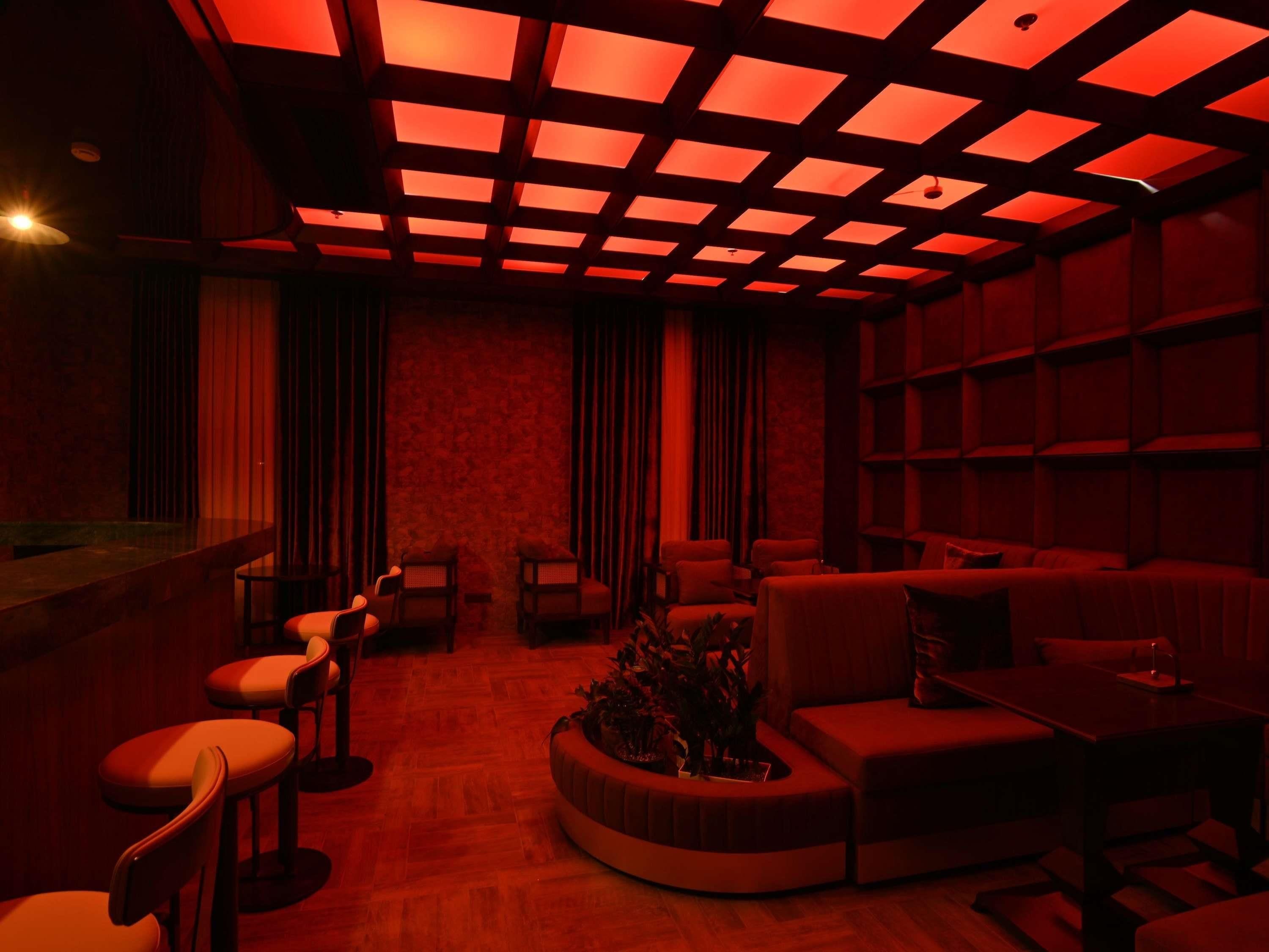 A dimly lit room with a red hue, featuring a bar area, seating arrangements, and a patterned wall.