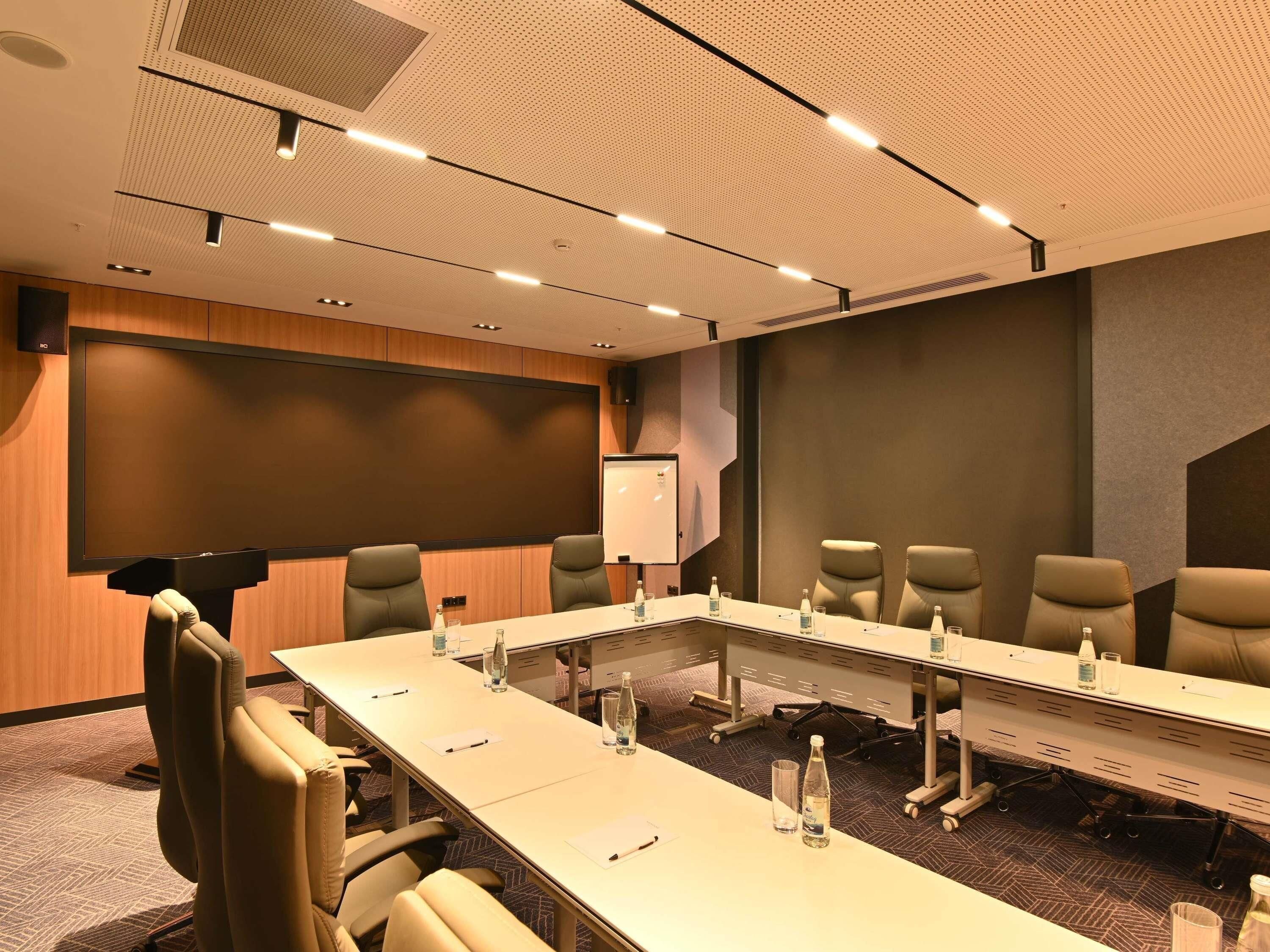 A conference room with a long table, chairs, a whiteboard, and a projector screen.