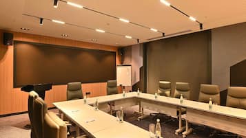 A conference room with a long table, chairs, a whiteboard, and a projector screen.