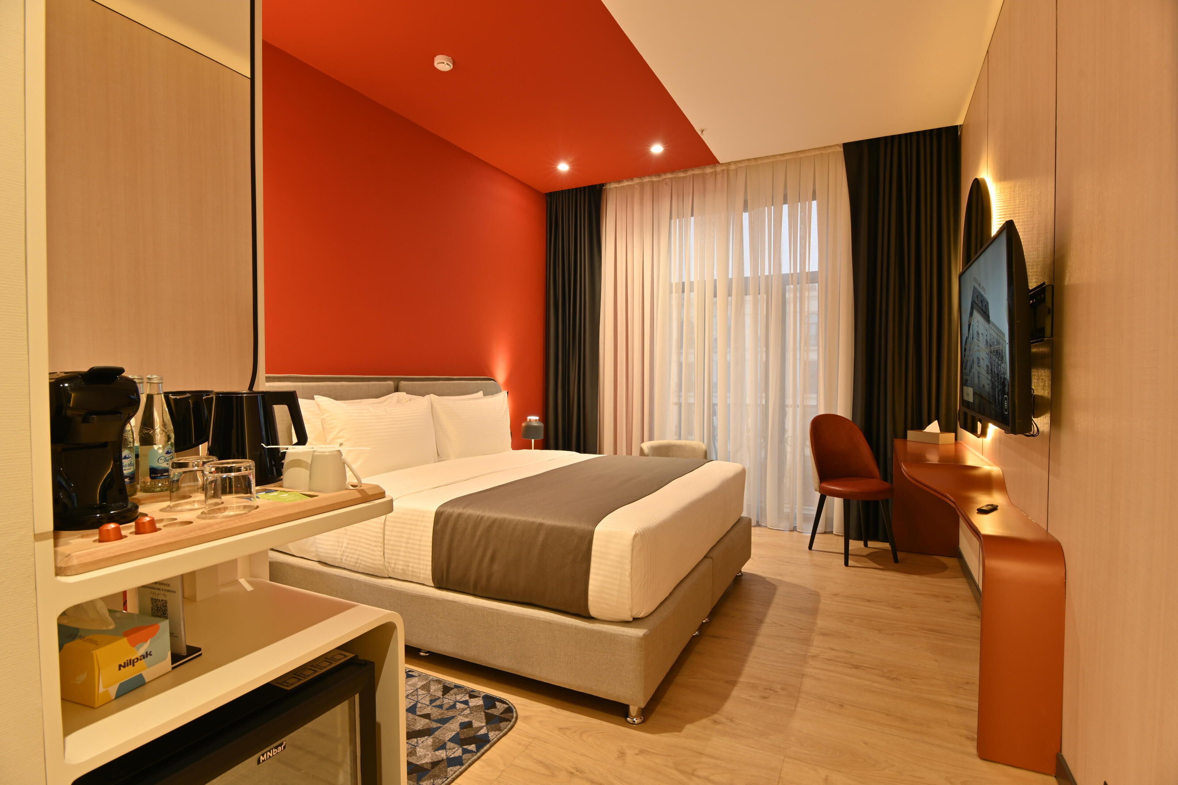A hotel room with a bed, a desk, a chair, a television, and a window with curtains.