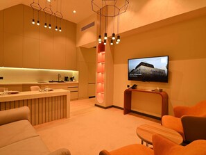 Un hall d’hôtel moderne doté d’un espace cuisine, d’un téléviseur affichant le nom de l’hôtel et de différents espaces pour s’asseoir.