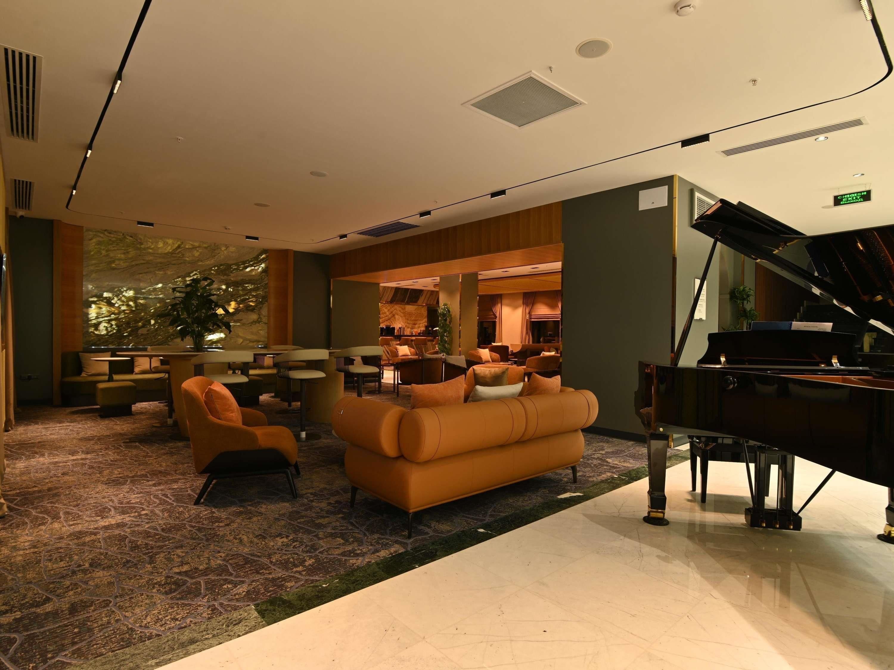 Un vestíbul d'hotel amb un piano de cua, seients confortables i un gran finestral.