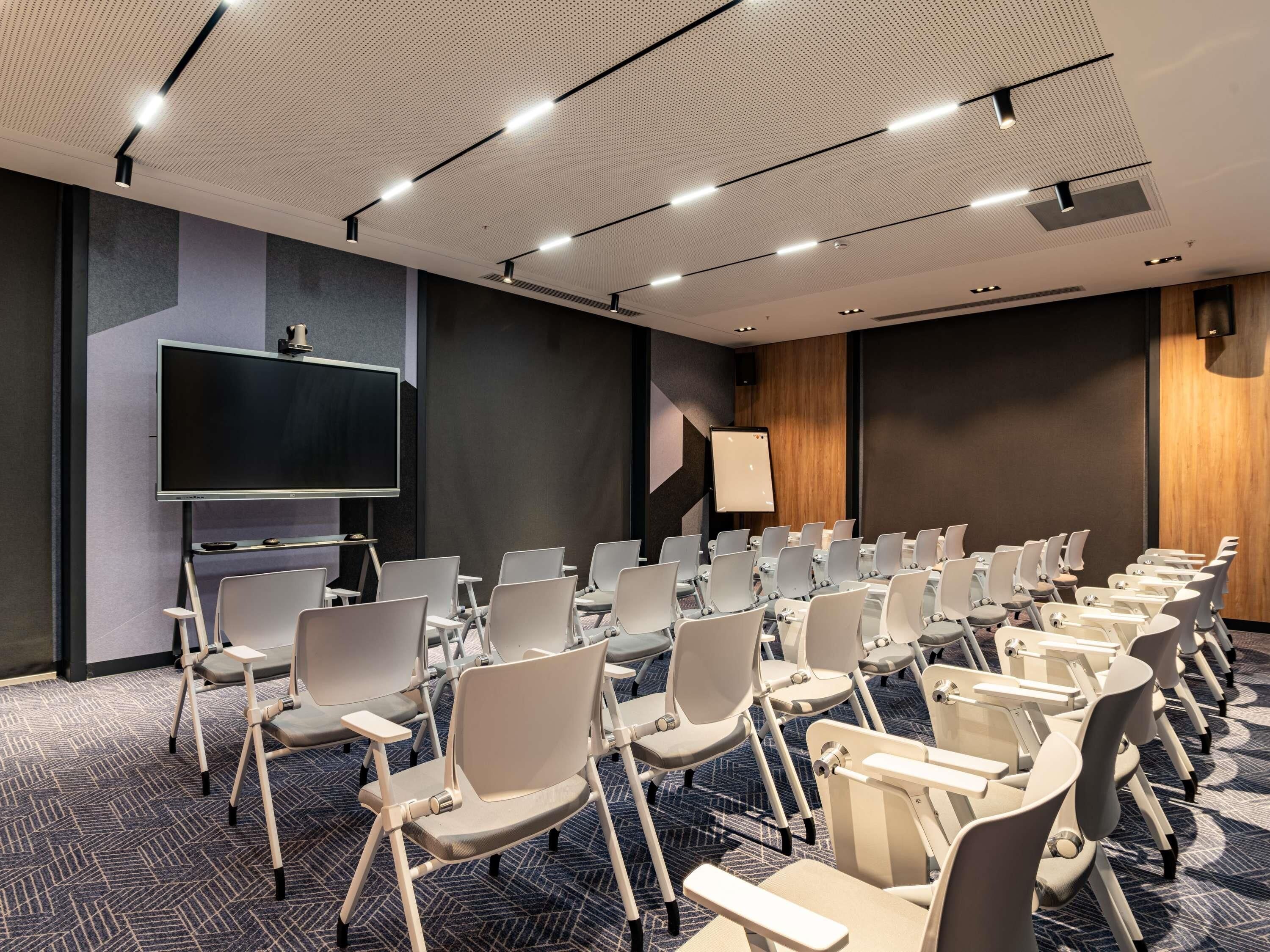 A conference room with rows of chairs, a large screen, and a whiteboard.