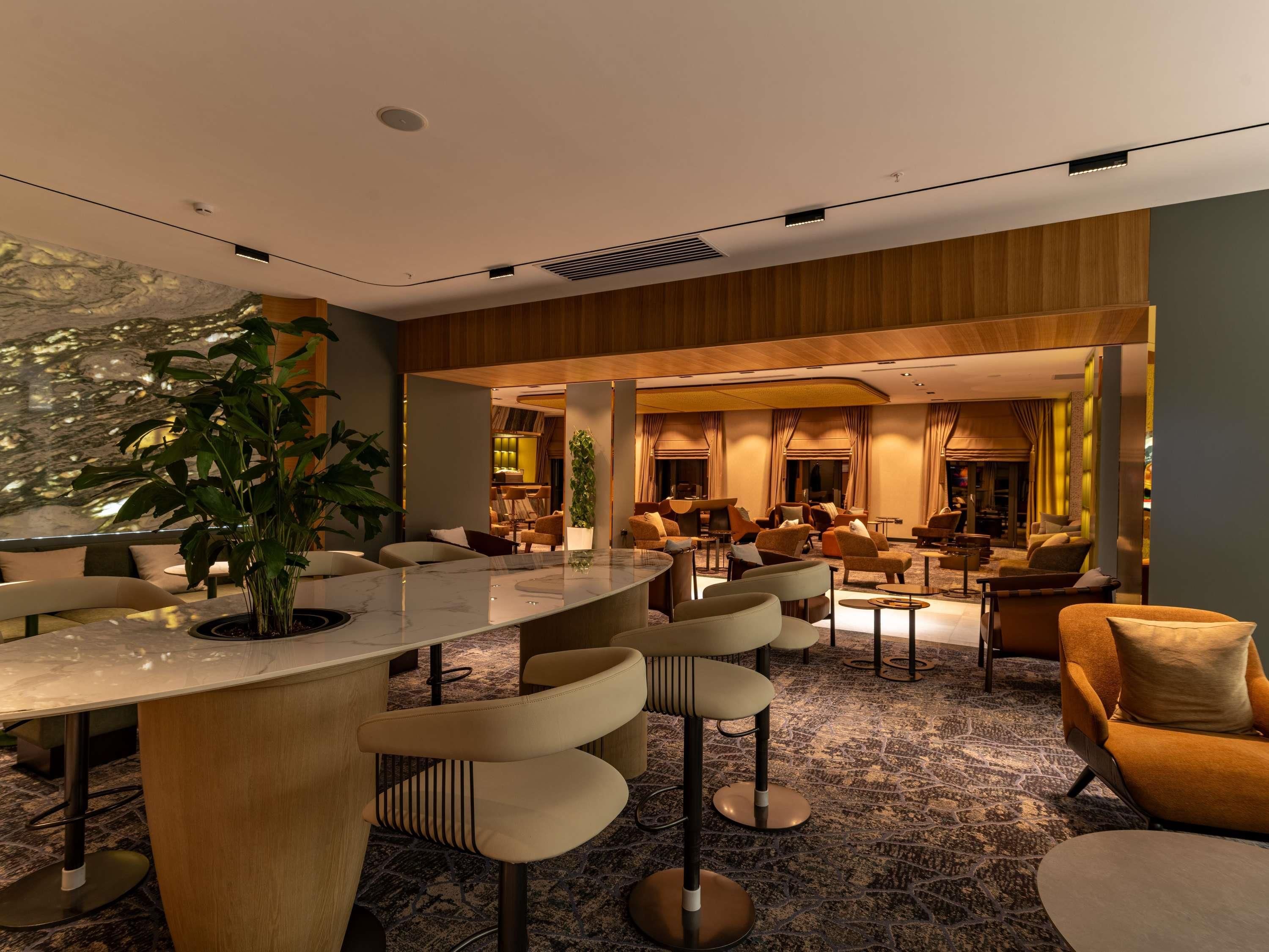 A modern hotel lobby with a marble reception desk, comfortable seating, and a large plant.