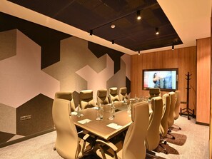 Un salón de conferencias con una gran mesa, varias sillas, una pantalla de televisión y un revestimiento de pared de madera.
