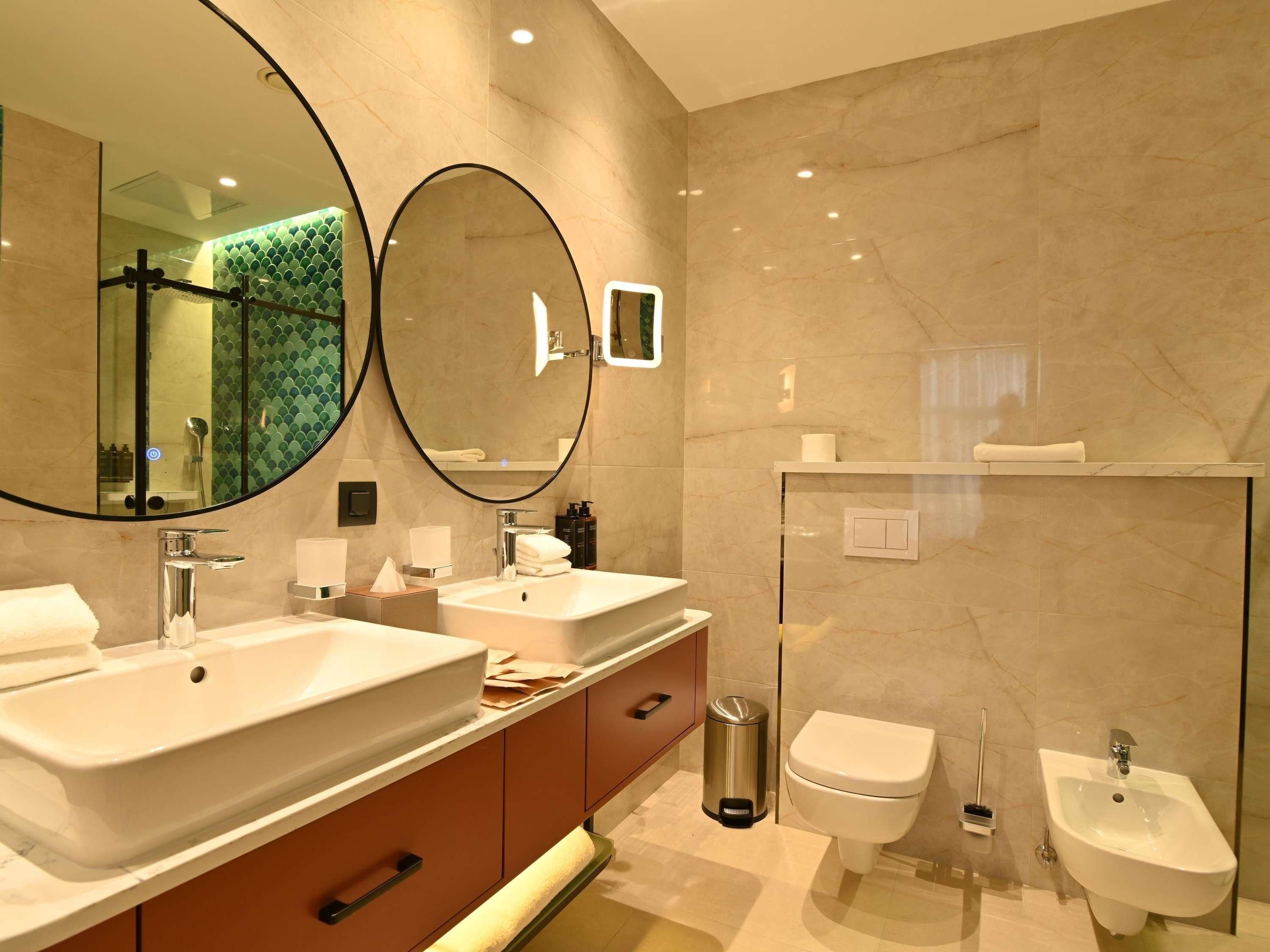 Een moderne badkamer met twee wastafels, toilet, bidet en een grote spiegel.
