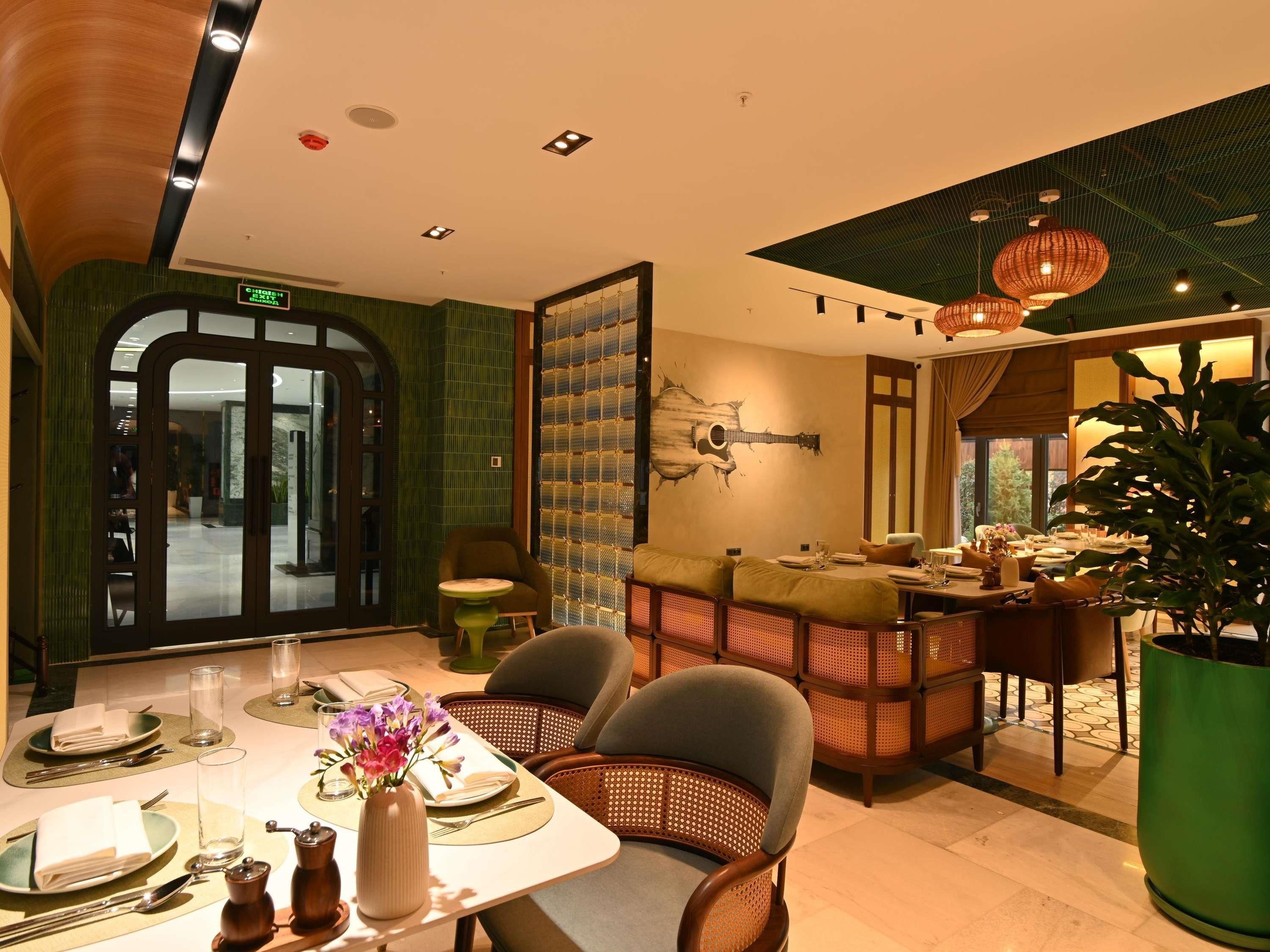A dining area with a table set for two, a green wall with a guitar mural, and a large potted plant.
