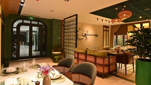 A dining area with a table set for two, a green wall with a guitar mural, and a large potted plant. - Mercure Tashkent North (Tashkent)