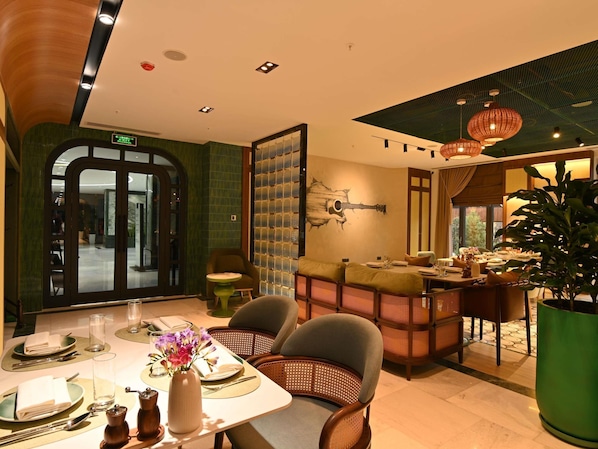 A dining area with a table set for two, a green wall with a guitar mural, and a large potted plant. - Mercure Tashkent North (Tashkent)