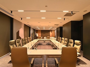 Uma sala de conferências com uma mesa comprida, várias cadeiras e um projetor.