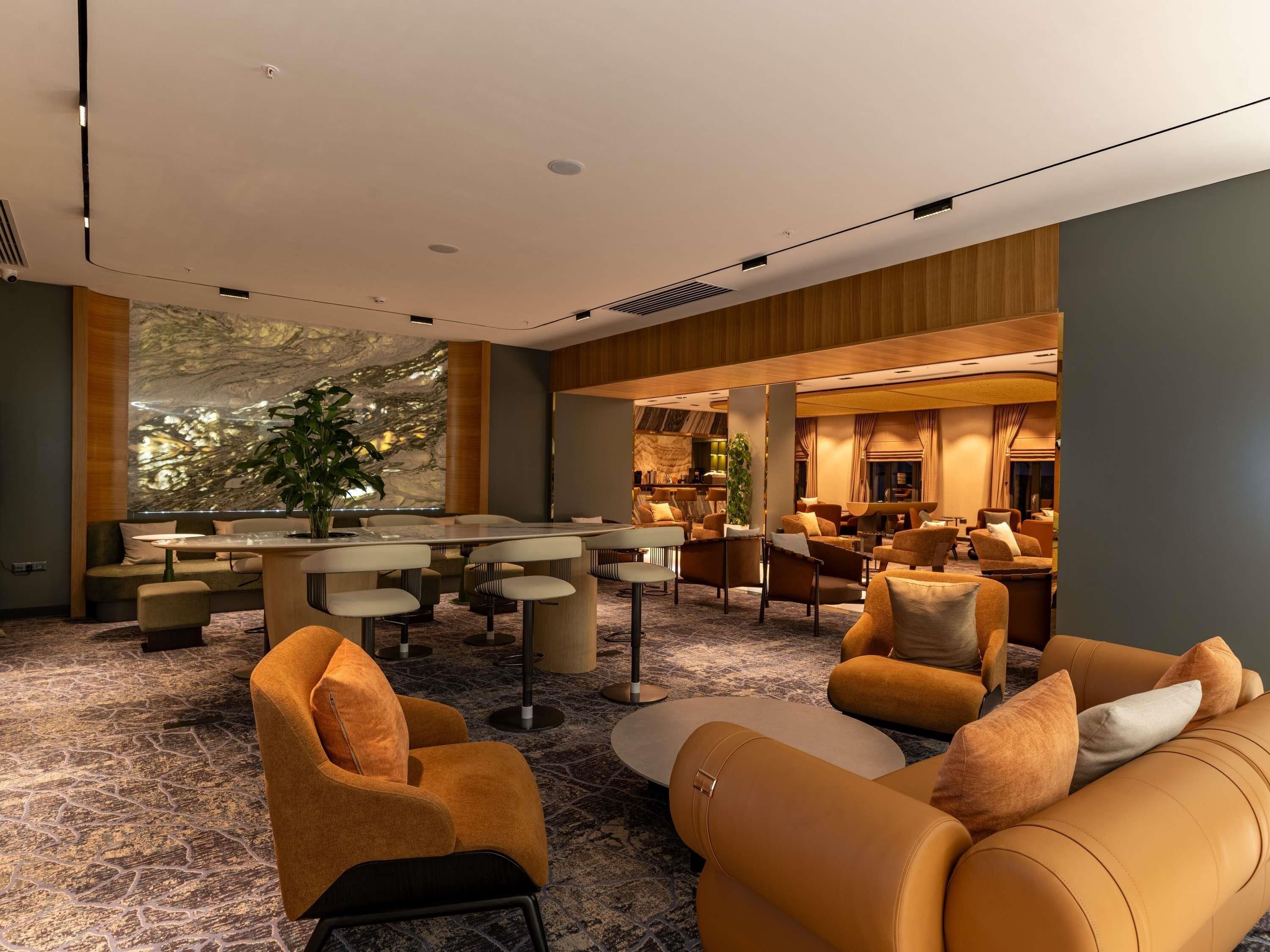 A modern hotel lobby with a marble wall, seating area, and a bar.
