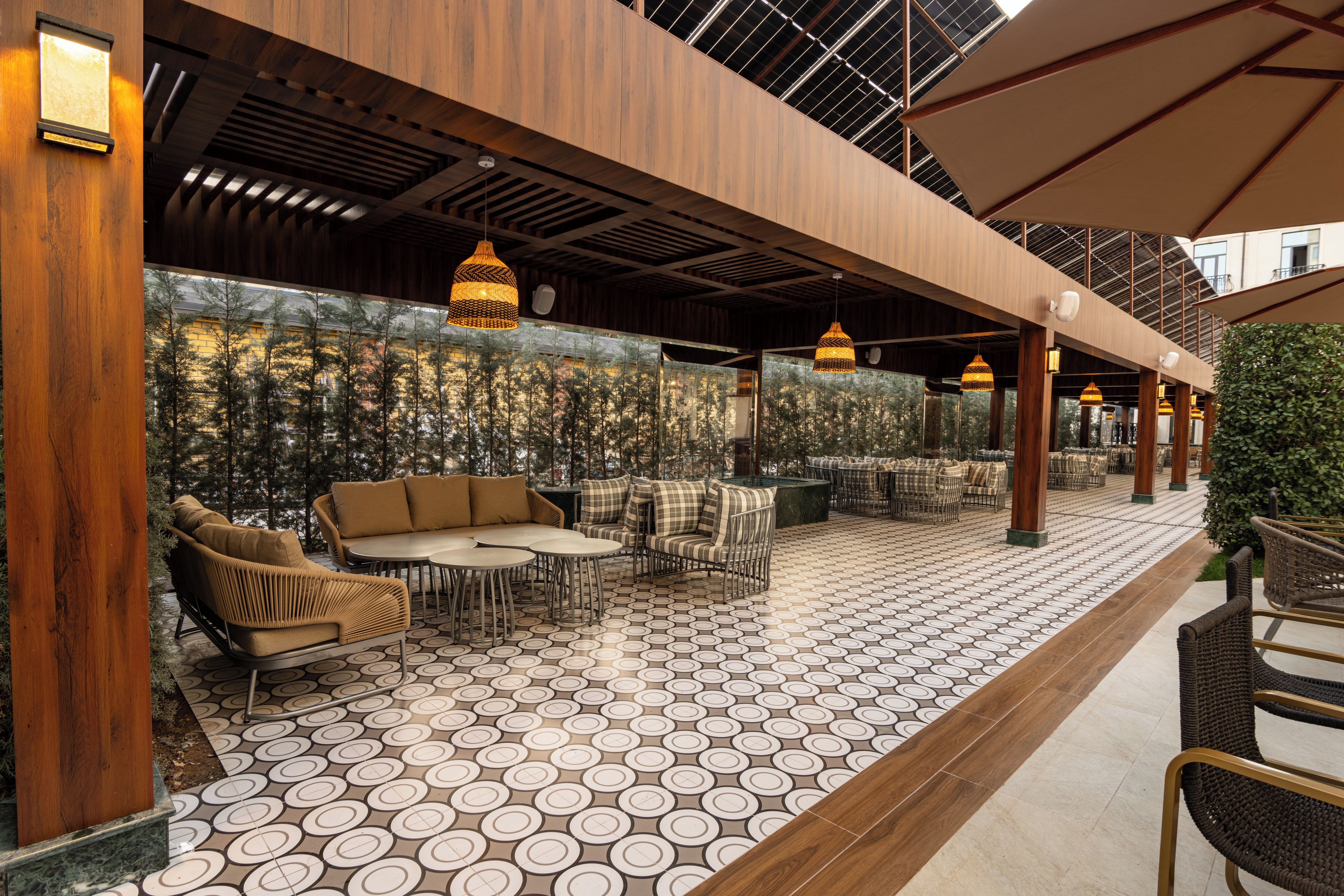 An outdoor seating area with round tables and wicker chairs, a patterned floor, and a wooden ceiling structure.