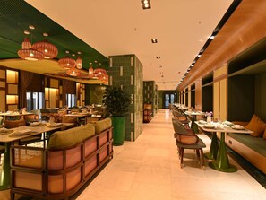 A restaurant with high ceilings, hanging wicker lamps, and a central green plant. Tables are set with white tablecloths and green chairs. - Mercure Tashkent North (Tashkent)