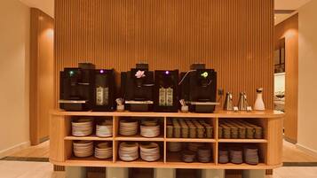 Un racó de cafè amb diverses màquines d'espresso, diferents tasses i platets, i un fons de panells de fusta.
