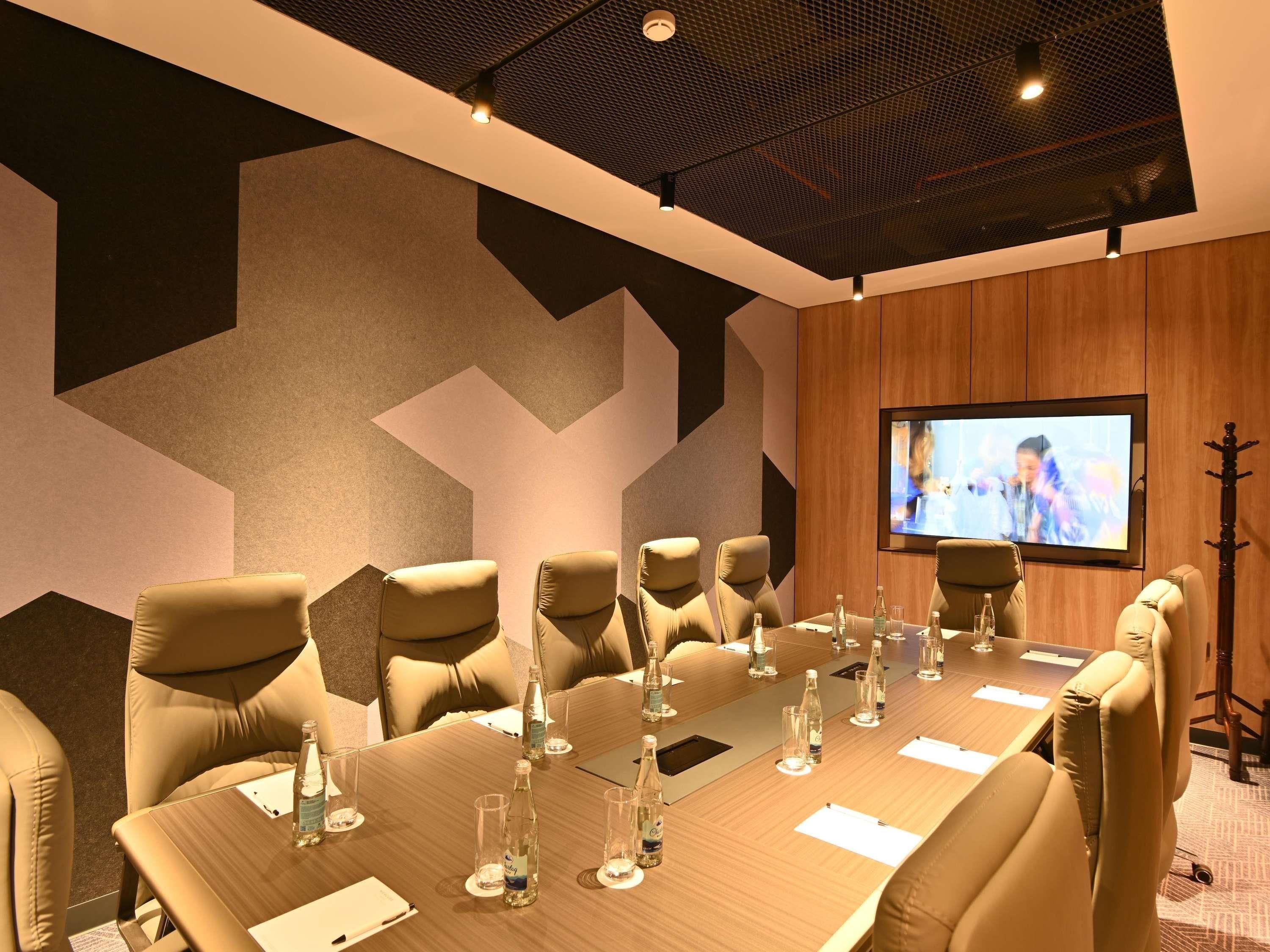 A conference room with a long table, multiple chairs, and a screen displaying a person.