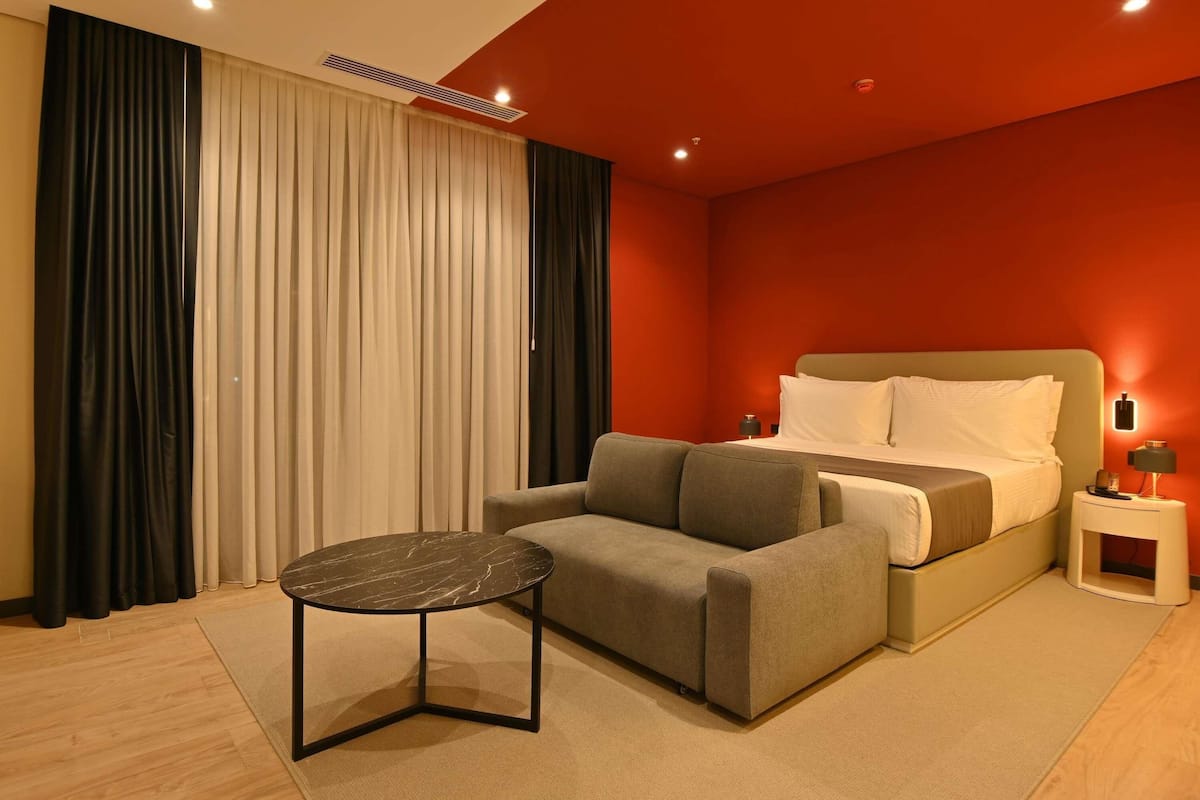 A hotel room with a bed, a sofa, a small table, and a nightstand.