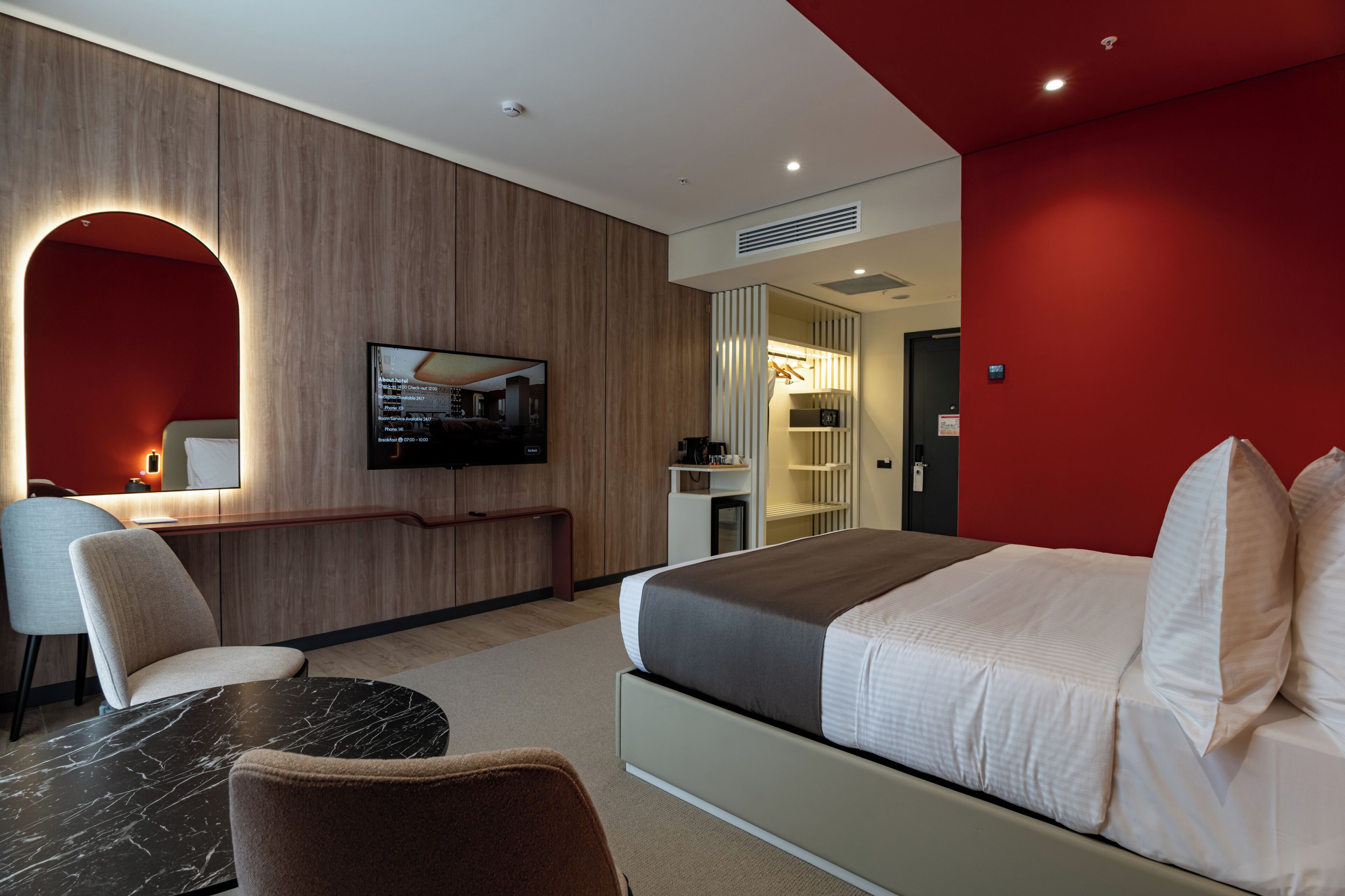 A hotel room with a bed, a desk, a chair, a TV, and a wardrobe.