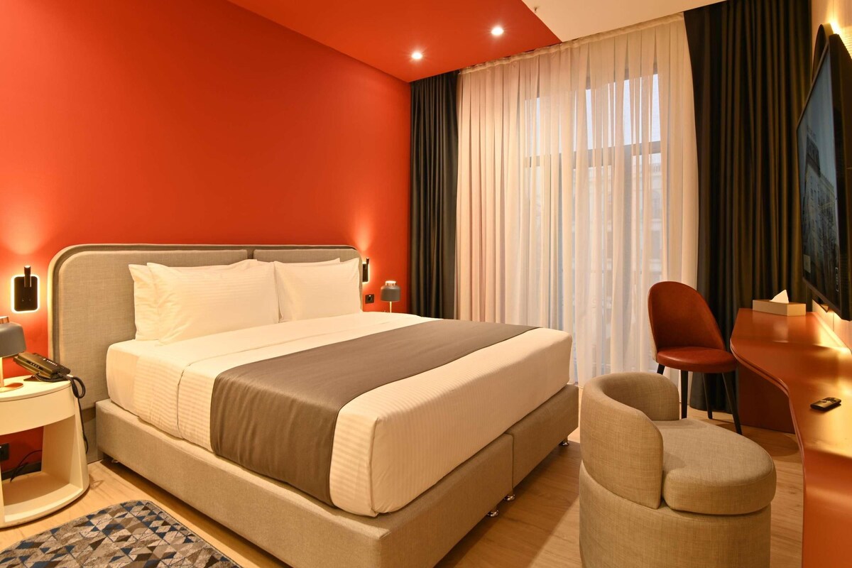 Habitación de hotel con cama, escritorio, silla y televisor.