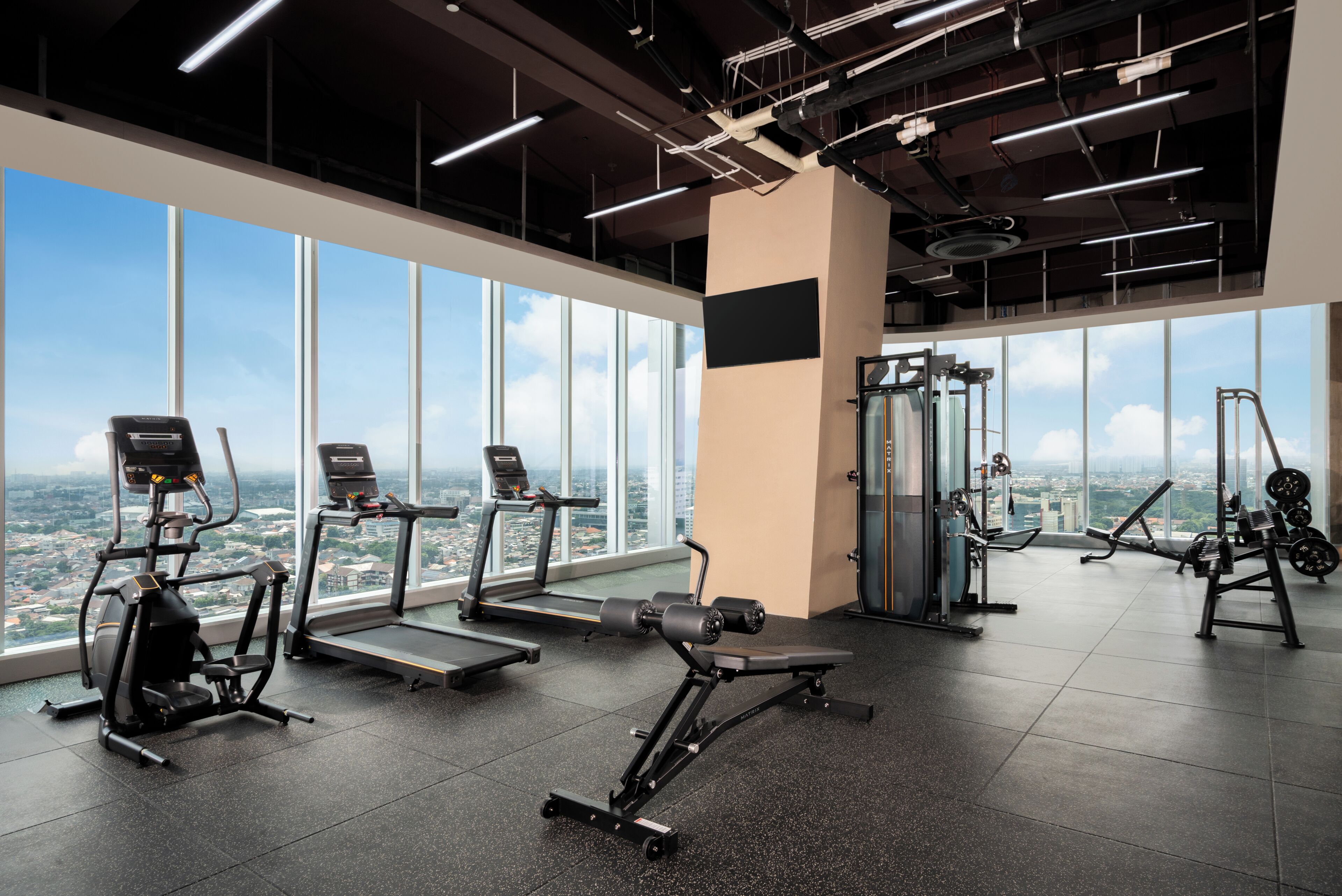 Un gimnasio con equipo de ejercicio, amplias ventanas y vista a la ciudad.