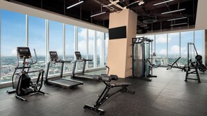 Et fitnesscenter med træningsudstyr, store vinduer og udsigt over byen.