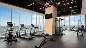 Un gimnasio con equipo de ejercicio, amplias ventanas y vista a la ciudad.