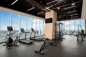 Ein Fitnessstudio mit Trainingsgeräten, großen Fenstern und Blick auf die Stadt.