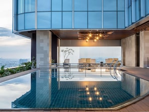 Ein modernes Gebäude mit einem Dachpool, Sitzgelegenheiten im Freien und Blick auf die Stadt.