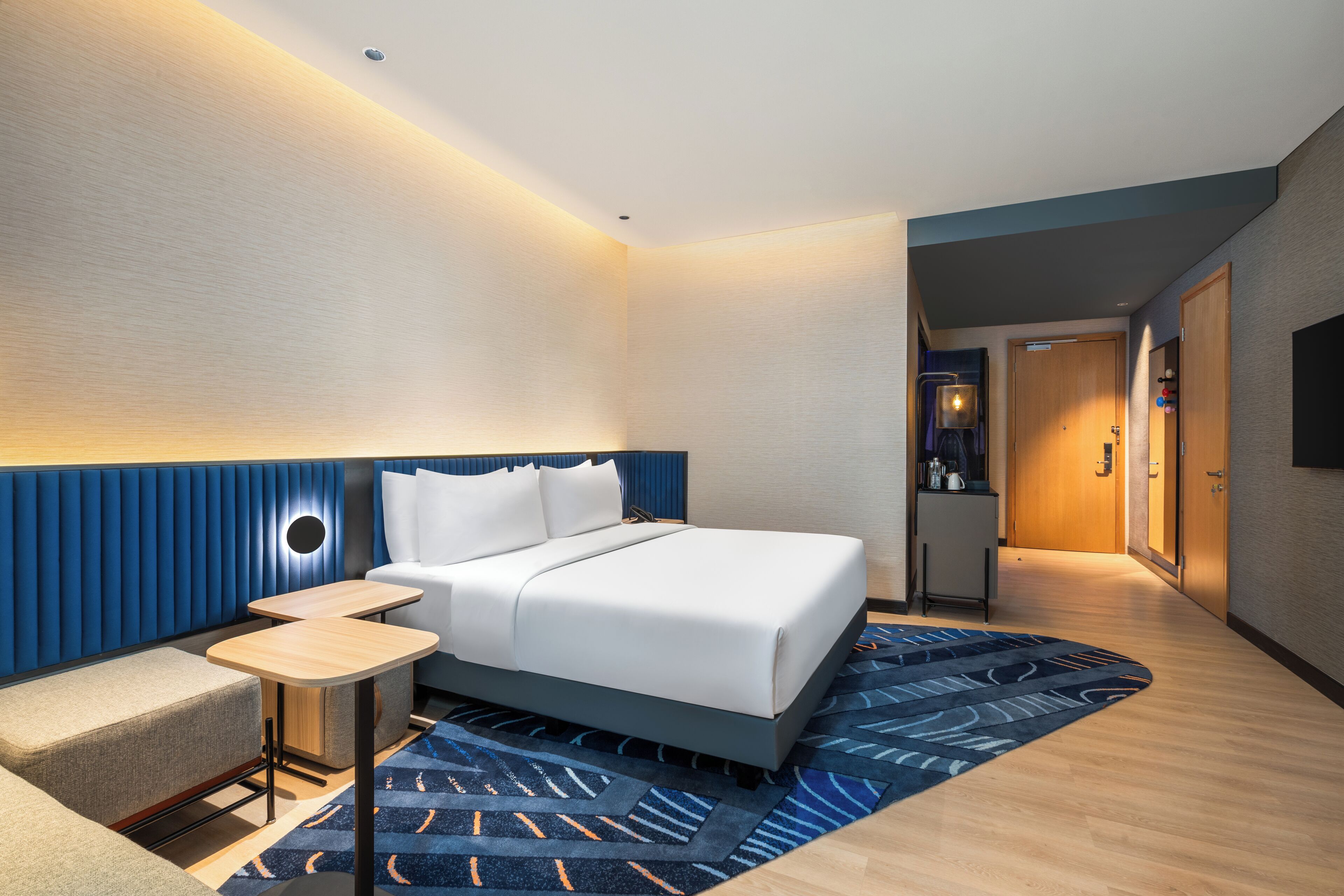 Une chambre d’hôtel moderne comprenant un lit, des tables de chevet, un petit coin salon et un couloir menant à la salle de bain.