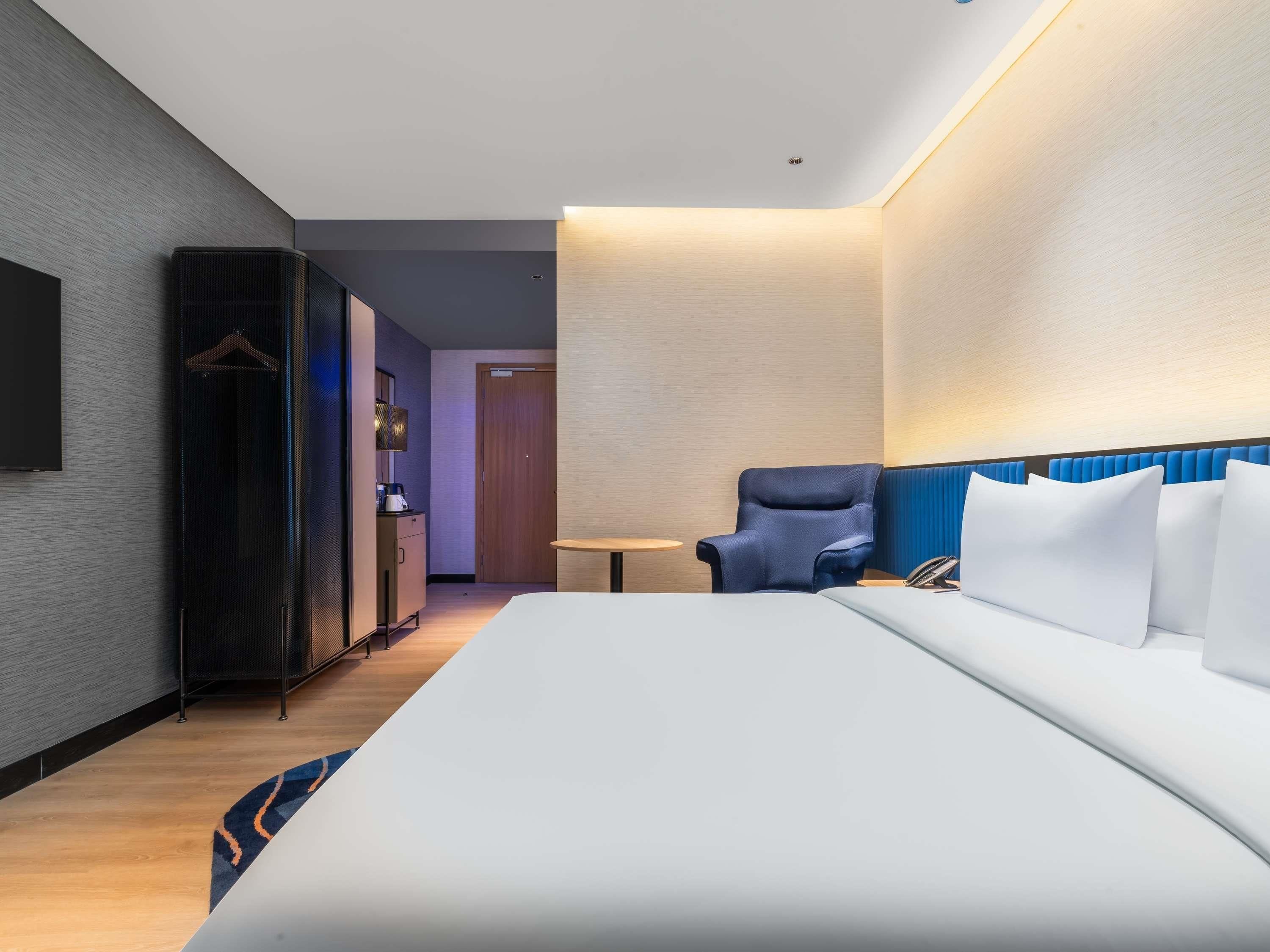 A hotel room with a bed, a chair, a desk, a wardrobe, and a door.