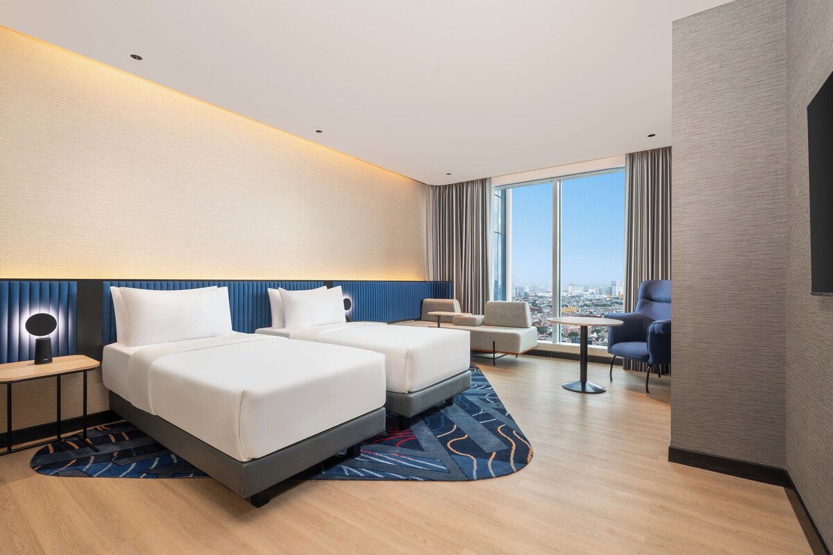 Ein modernes Hotelzimmer mit zwei Betten, einem Schreibtisch und Blick auf die Stadt.