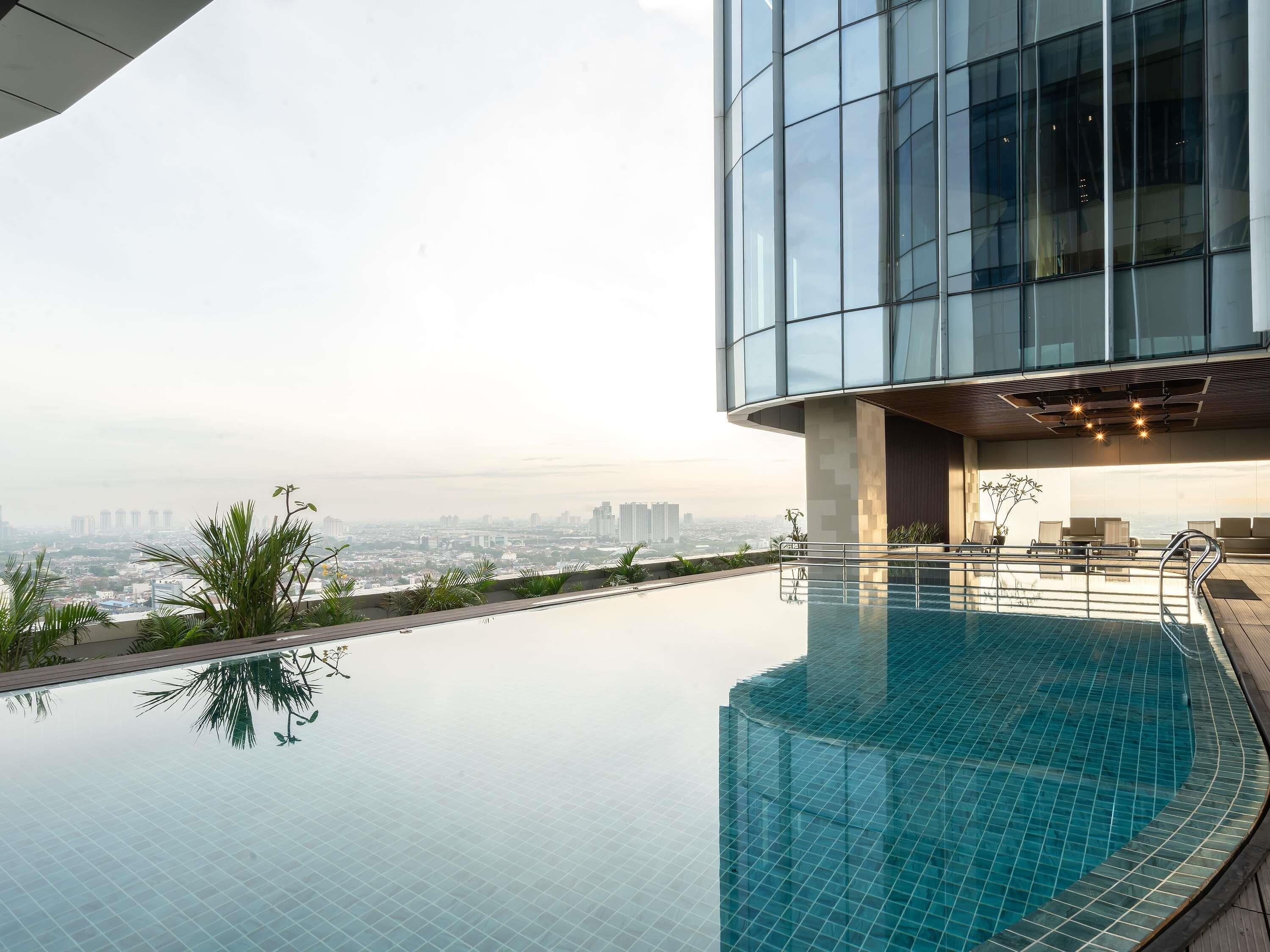 Um edifício moderno com piscina infinita no terraço, oferecendo vista para a cidade.