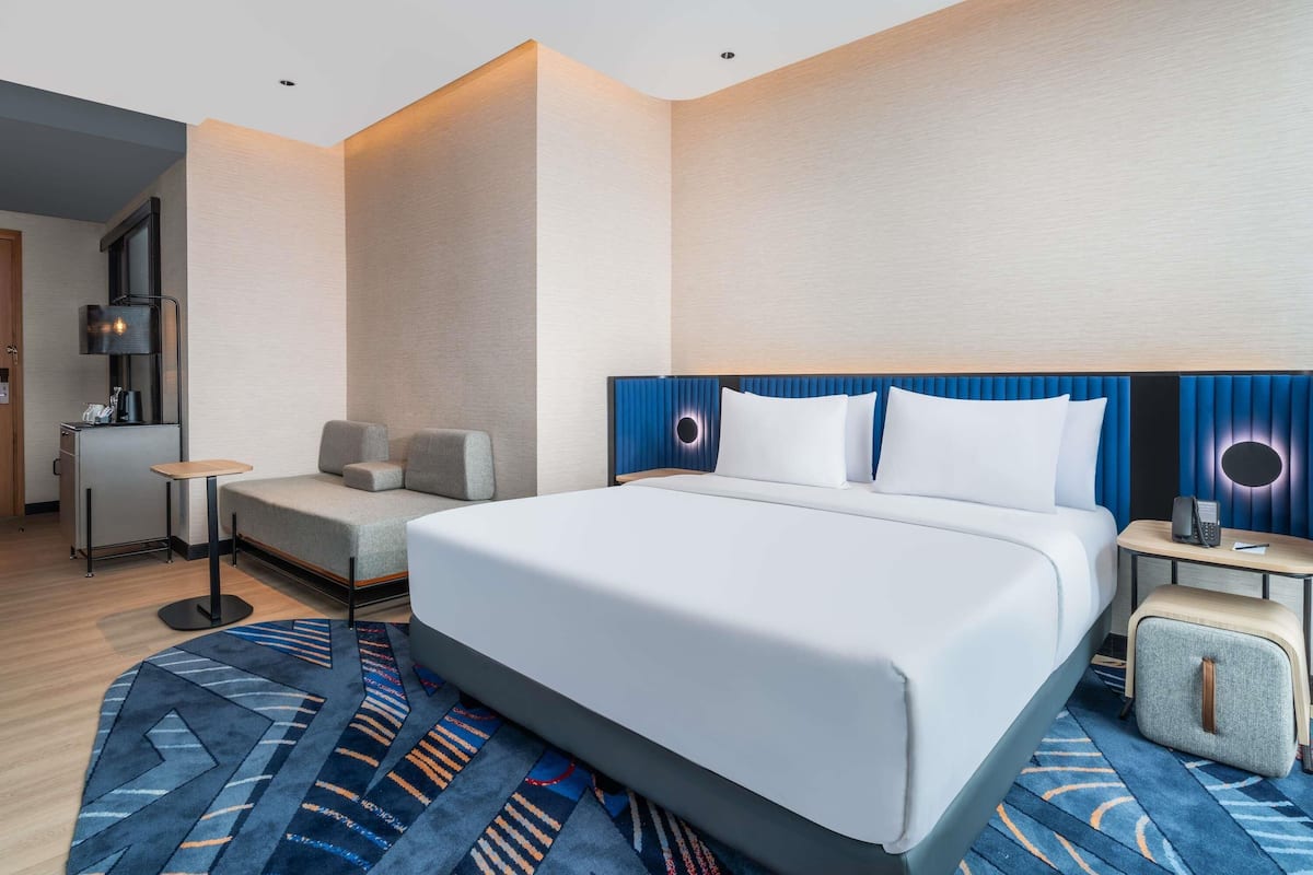 Una habitación de hotel moderna con una cama grande, un escritorio, una silla y un pequeño rincón de descanso.