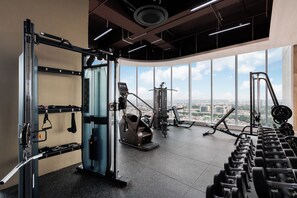 Ein Fitnessstudio mit Trainingsgeräten, großen Fenstern und Blick auf die Stadt.