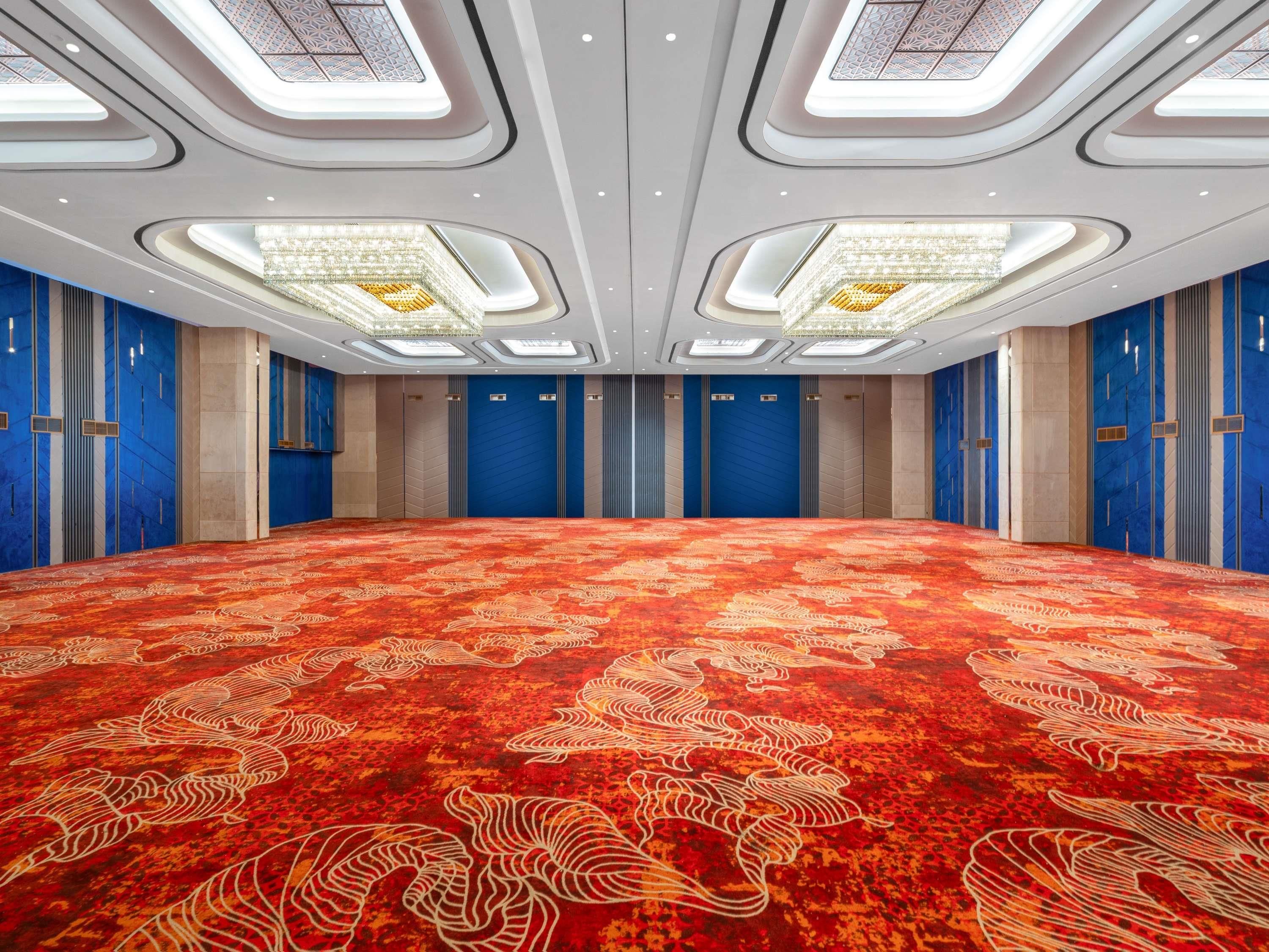 Un'ampia sala conferenze con tappeto a motivi, pareti blu e un alto soffitto con lucernari.