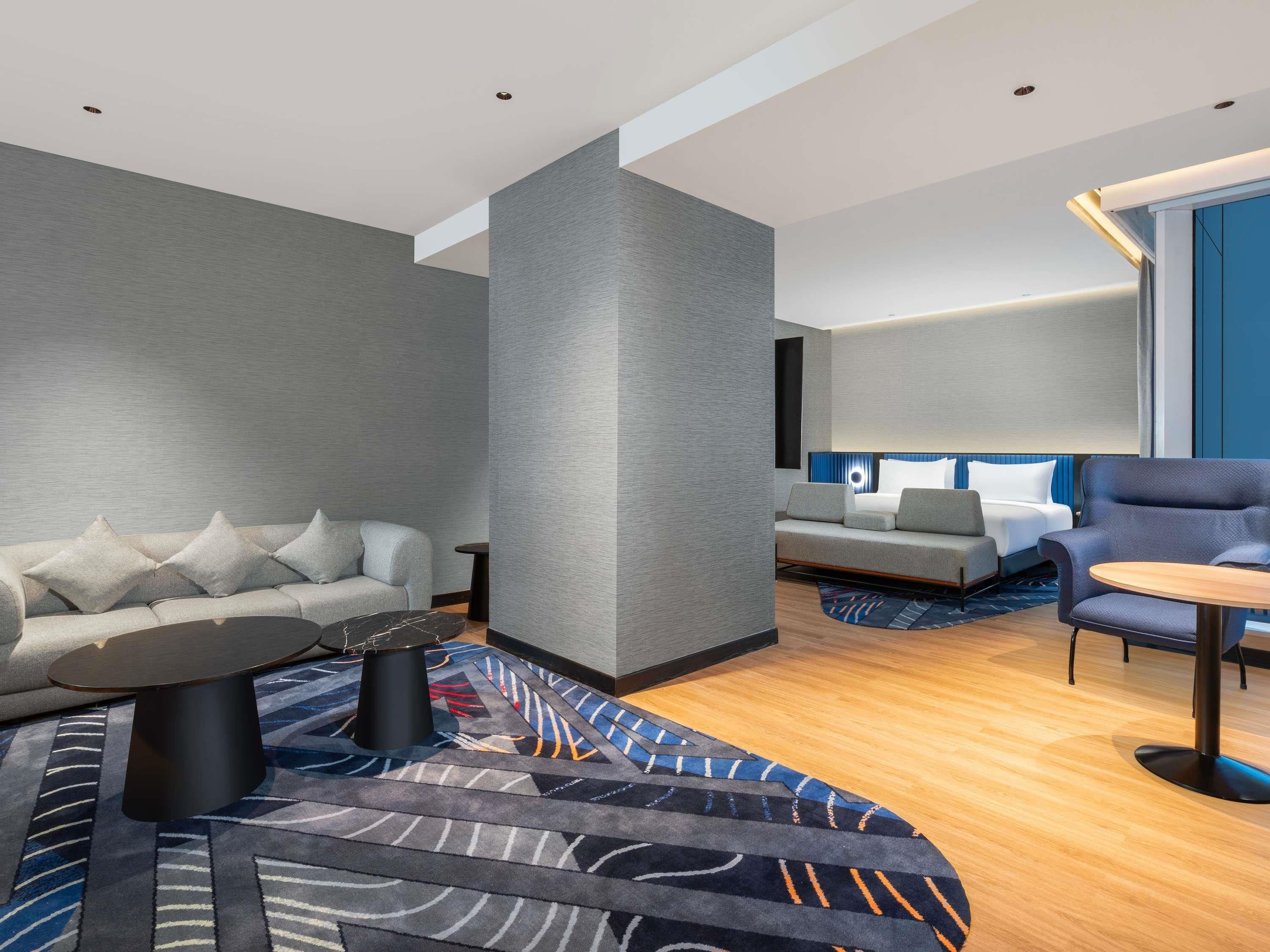 A modern hotel room with a grey sofa, a round coffee table, and a blue armchair.