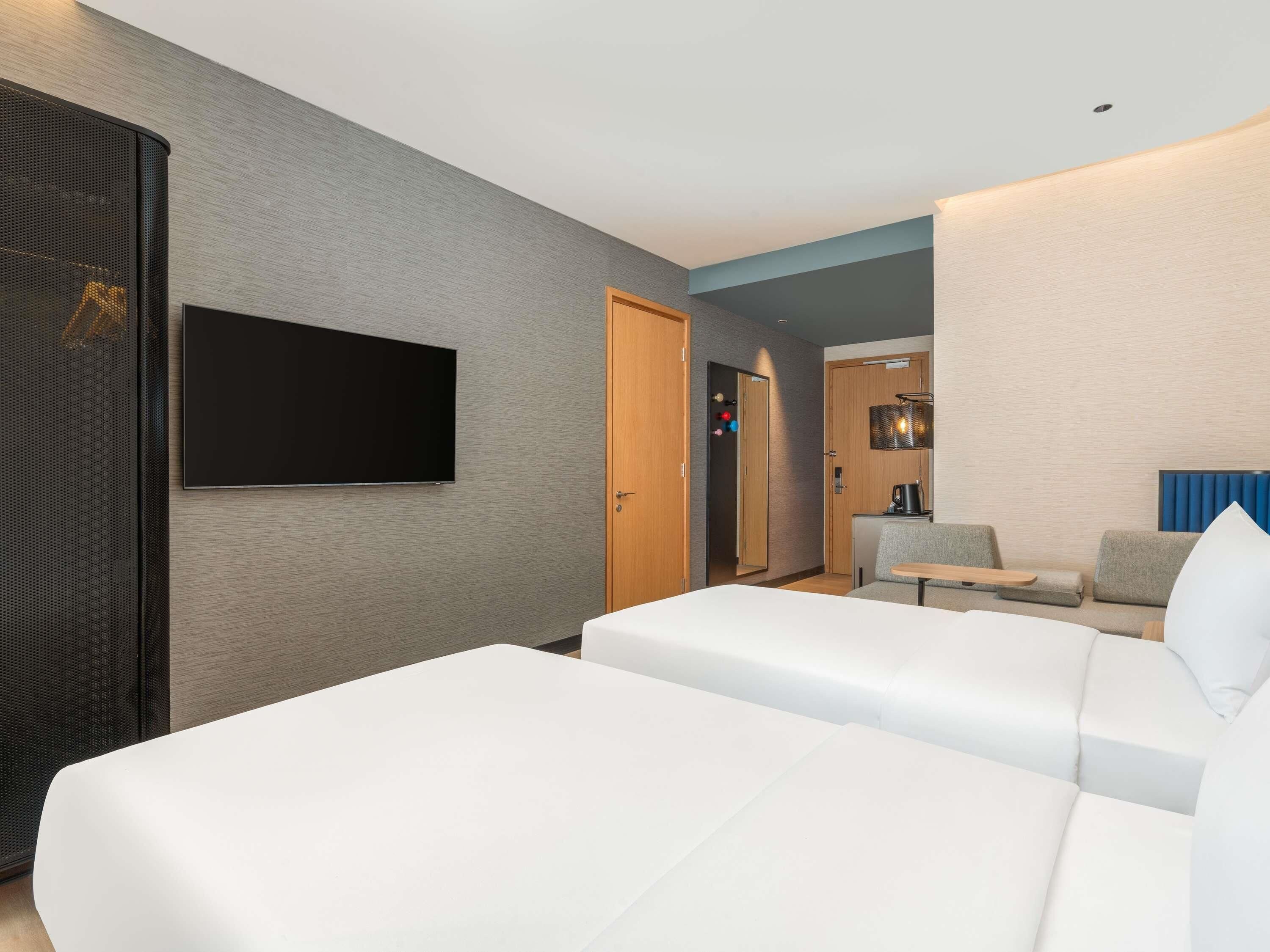A hotel room with a TV, a sofa, a small table, and a kitchenette area.