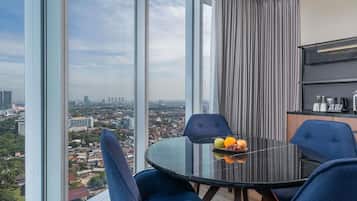 A modern room with a glass table, blue chairs, a fruit bowl, and a city view.