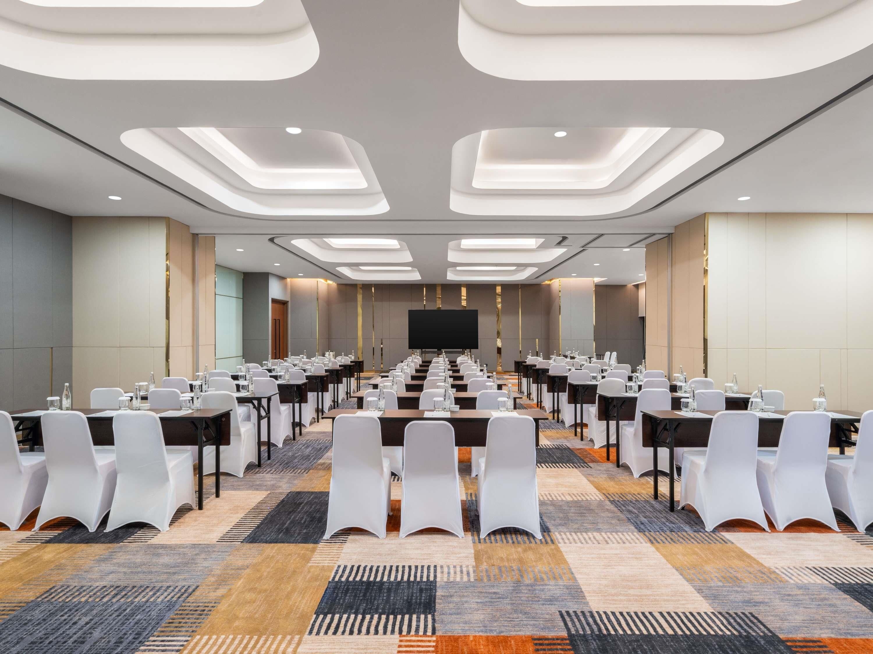 Una sala conferenze con un lungo tavolo, sedie bianche e pavimento rivestito di moquette.