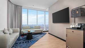 A modern hotel room with a sofa, a coffee table, a TV mounted on the wall, and a city view. - Novotel Jakarta Pulo Mas (Jakarta)