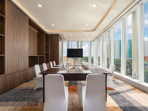A conference room with a long table, white chairs, a flat-screen TV, and large windows offering a city view. - Novotel Jakarta Pulomas (Jakarta)
