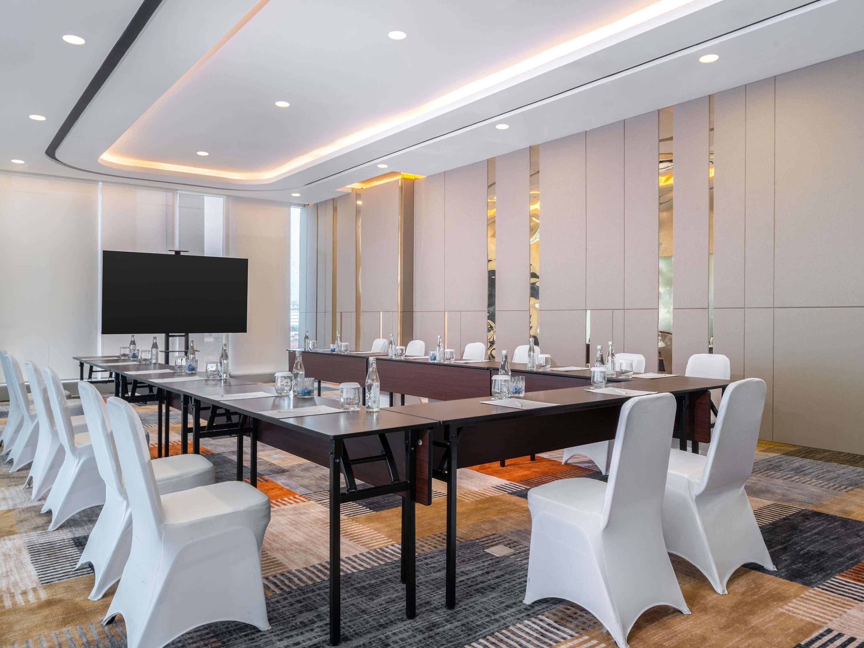 A conference room with a long table, white chairs, a flat-screen TV, and a carpeted floor.