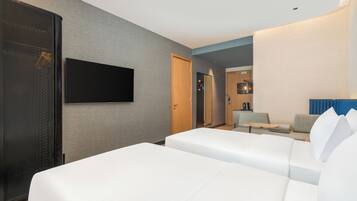 A hotel room with two beds, a TV, a kitchenette, and a seating area.