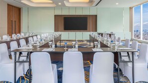 A conference room with a long table, white chairs, and a large screen. - Novotel Jakarta Pulo Mas (Jakarta)